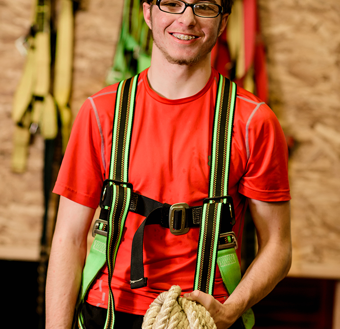 Male student holding rope and wearing rooftop harness system