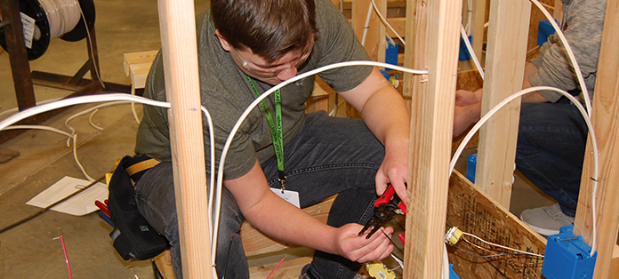 Male student working on stud wall installing electrical outlet wiring.