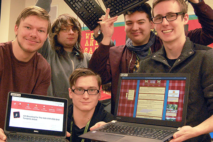 five smiling students, two laptops showing websites that have been designed by students.